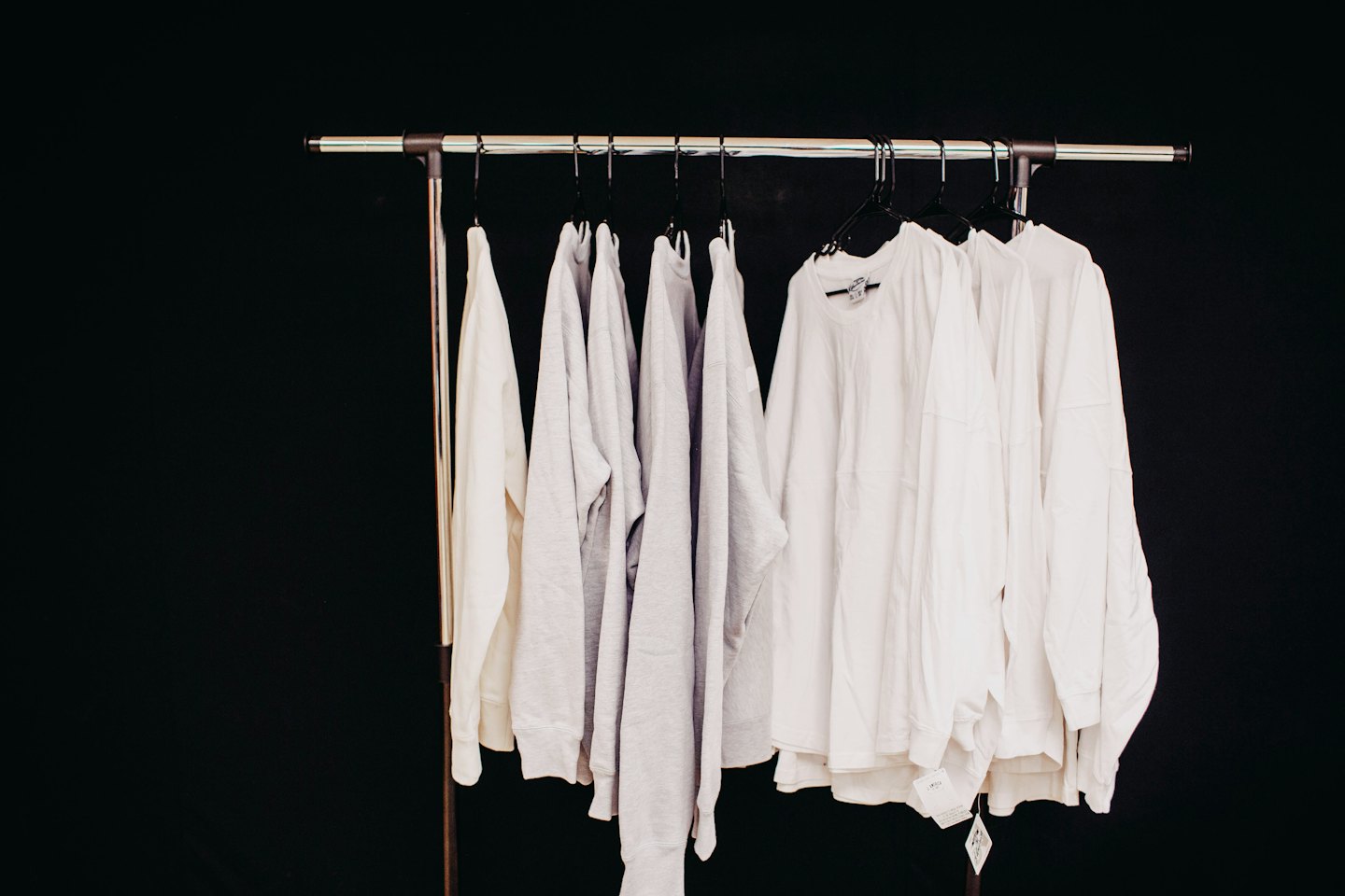 Metal clothing rack with white and grey shirts on black hangers.