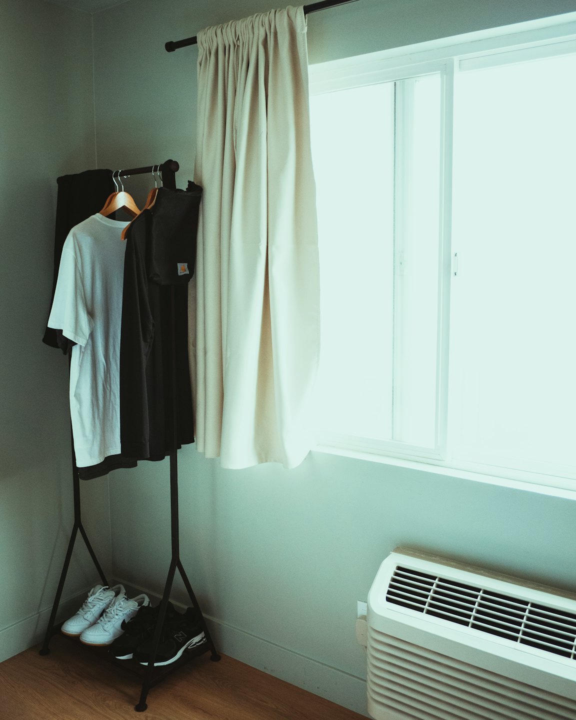 Minimalist clothing rack with shirts and sneakers in a room.